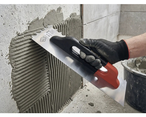 Tegellijm aanbrengen op een muur met een roestvrijstalen troffel