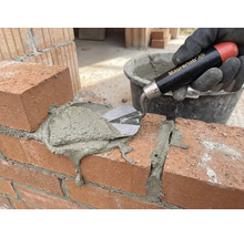 Een hand met handschoen brengt met een troffel mortel aan op een bakstenen muur