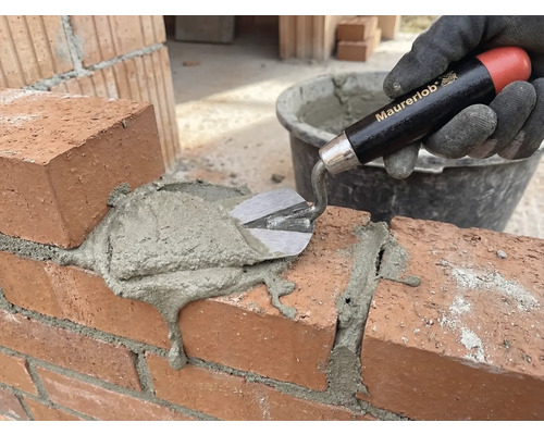 Een hand met handschoen brengt met een troffel mortel aan op een bakstenen muur