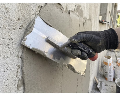 Ambachtsman maakt stucwerk glad met een pleisterspaan op een muur.