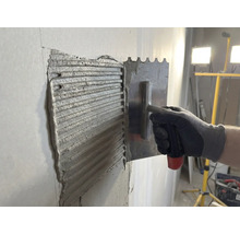 Tegellijm wordt met een roestvrijstalen spaan op een muur aangebracht