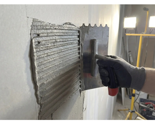 Tegellijm wordt met een roestvrijstalen spaan op een muur aangebracht