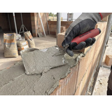 Metselaar werkt met een troffel aan een bakstenen muur, op de achtergrond zakken cement.