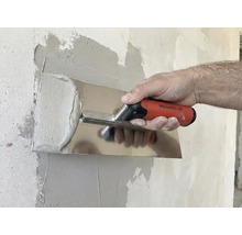 Iemand strijkt gips glad met een pleisterspaan op een muur.