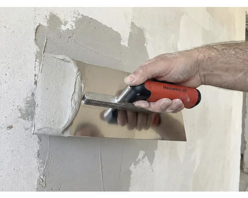 Iemand strijkt gips glad met een pleisterspaan op een muur.