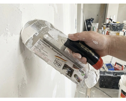 Gladde spaan Superglatt met handvat in de hand bij het pleisteren van een muur