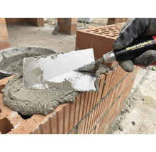 Metselaar met troffel die mortel aanbrengt op bakstenen voor metselwerk