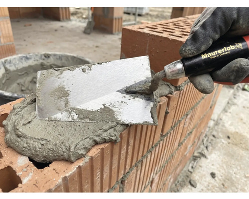 Metselaar met troffel die mortel aanbrengt op bakstenen voor metselwerk