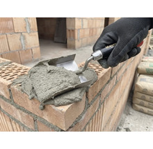 Metselaars hand met troffel brengt mortel aan op bakstenen