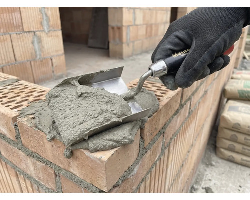 Metselaars hand met troffel brengt mortel aan op bakstenen