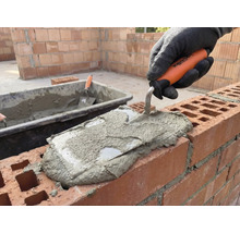 Metselaar brengt met een troffel mortel aan op een muur.