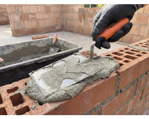 Metselaar brengt met een troffel mortel aan op een muur.