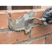 Metselaar die een bakstenen muur voegt met een troffel
