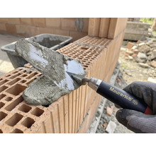 Hand van metselaar met troffel die mortel aanbrengt op bakstenen