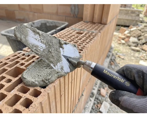 Hand van metselaar met troffel die mortel aanbrengt op bakstenen