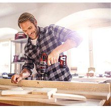 Een man boort een houten plank met een accuboormachine.