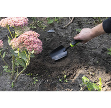 Tuinscene met hand die een plantenschep in de grond steekt