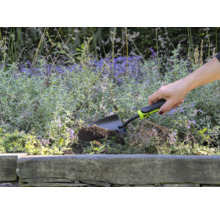 Iemand gebruikt een kleine tuinschep om in een bloembed te graven.