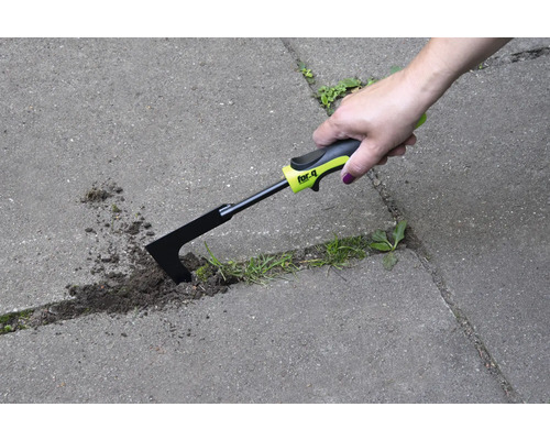 Een hand gebruikt een voegenkrabber om onkruid te verwijderen tussen bestratingstenen.