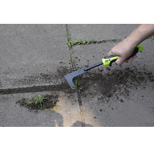 Een persoon verwijdert onkruid met een voegenkrabber op een verhard oppervlak.