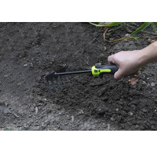 Hand houdt een kleine hark in de tuingrond