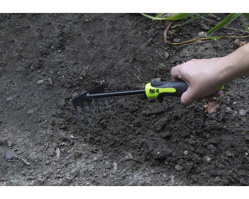 Hand houdt een kleine hark in de tuingrond