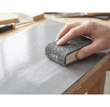 Een hand schuurt een gelakt houten oppervlak met een schuurvlies dat om een schuurblok is gewikkeld.