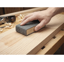Hand schuurt een houten plank met een schuurvlies op een schuurblok.