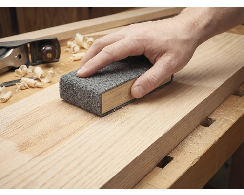 Hand schuurt een houten plank met een schuurvlies op een schuurblok.