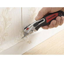 Hand met Rautner afbreekmes bij het nauwkeurig afsnijden van behang met bloemmotief langs een plint.