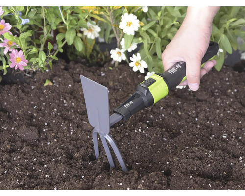 Hand hanteert een for_q handhak met tanden en blad in donkere aarde naast bloemen om de grond los te maken.