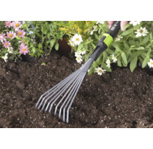 Handmatige kleine bladhark van for_q wordt gebruikt in donkere tuinaarde naast roze en witte bloemen.