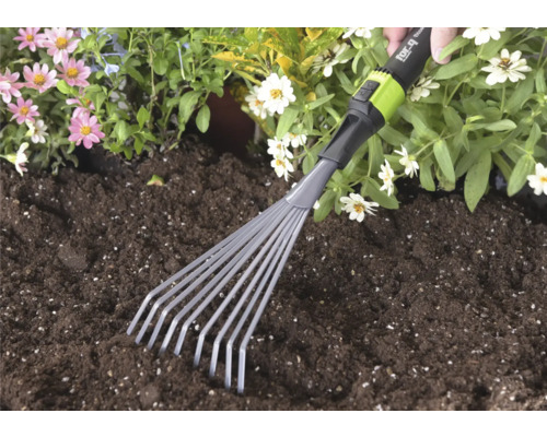 Handmatige kleine bladhark van for_q wordt gebruikt in donkere tuinaarde naast roze en witte bloemen.