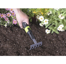 Handhark met zwart en groen handvat en for_q Logo wordt gebruikt in donkere potgrond tussen roze en witte bloemen.