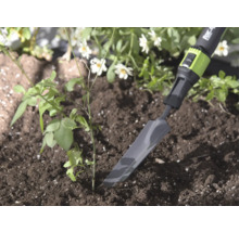 Smalle metalen verplantschop van for_q in de aarde naast een kleine plant, lichte en natuurlijke tuinomgeving.