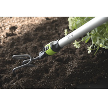 Tuinklauw met steel woelt aarde los naast planten.