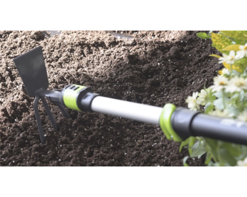 Handhak met metalen blad en drie tanden in donkere tuingrond naast bloemen.