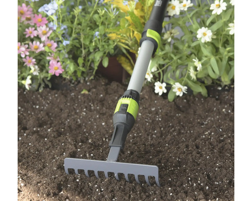 Kleine tuinhark met grijze metalen kop en verstelbare telescopische steel in donkere aarde voor bloemen.