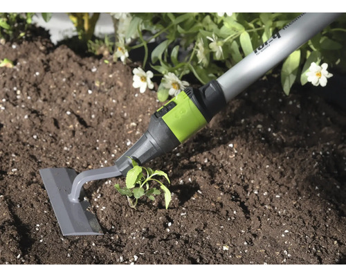 Tuinschoffel met grijs blad en groene aansluiting bij het wieden van onkruid in donkere aarde naast een plant.