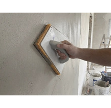 Hand gebruikt een sponsspaan op een vers gestucte muur.