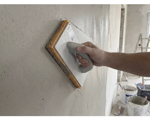 Hand gebruikt een sponsspaan op een vers gestucte muur.