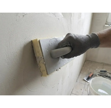 Hand met werkhandschoen gebruikt een sponsspaan voor het gladstrijken van stucwerk op een muur.
