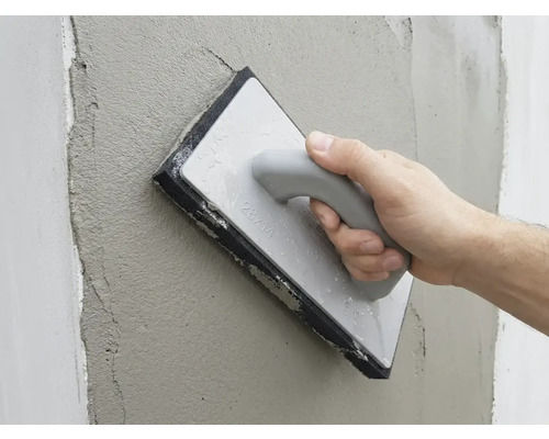 Hand strijkt vers pleisterwerk op een muur glad met een sponsbord.