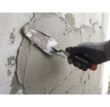 Een hand met werkhandschoen brengt mortel aan op een muur met een Maurerlob troffel.