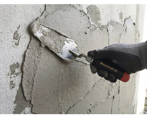 Een hand met werkhandschoen brengt mortel aan op een muur met een Maurerlob troffel.