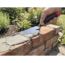 Hand met Maurerlob troffel brengt mortel aan op een bakstenen muur in de tuin.