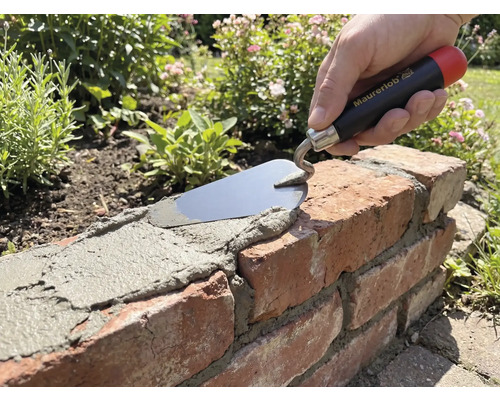 Hand met Maurerlob troffel brengt mortel aan op een bakstenen muur in de tuin.