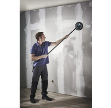 Een man schuurt een gipsplaatwand met een langnekschuurmachine met telescoopsteel.