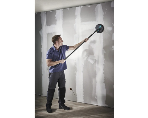 Een man schuurt een gipsplaatwand met een langnekschuurmachine met telescoopsteel.