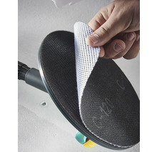 Een hand bevestigt een witte gaasschuurschijf op de zwarte ronde schuurzool van een wandschuurmachine.